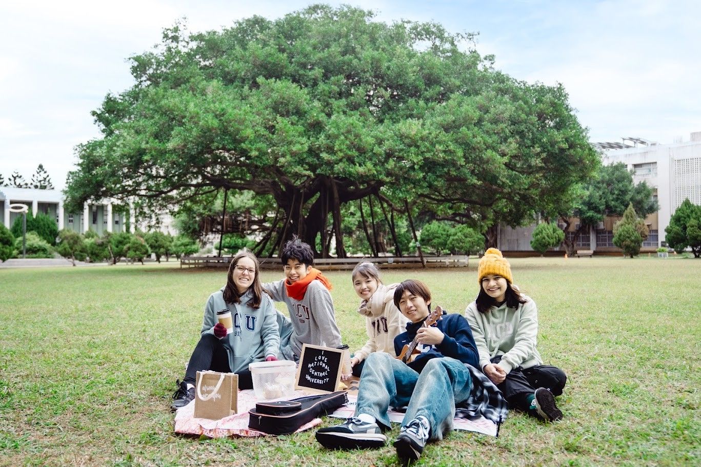 五位學生在中央大學校園的大榕樹下草地上野餐
